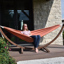Load image into Gallery viewer, Closer view of a person relaxing in a Coral hammock, showing the curved pine stand and white suspension ropes.