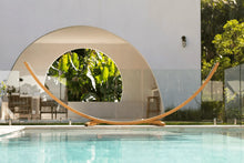 Load image into Gallery viewer, Front view of the 12ft larch wood arc hammock stand beside a swimming pool