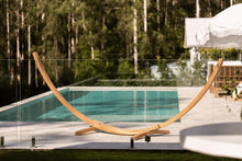 Load image into Gallery viewer, Larch wood arc hammock stand with hanging chains on a poolside patio overlooking trees