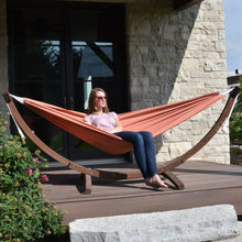 Load image into Gallery viewer, Person sitting in a Coral hammock on a solid pine arc stand on a sunny deck.