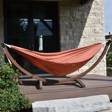 Load image into Gallery viewer, Coral Sunbrella® hammock on a solid pine arc stand on an outdoor deck beside a stone wall.