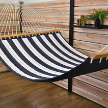 Load image into Gallery viewer, Angled view of the Harbour quilted hammock showing its striped bed and navy underside on a timber deck.