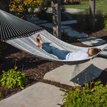 Load image into Gallery viewer, Woman stretched out in a Dove quilted hammock above a garden path.