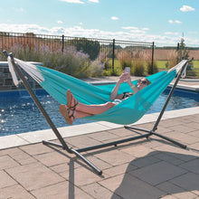 Load image into Gallery viewer, Person relaxing in a turquoise Aruba hammock on a metal stand beside a swimming pool