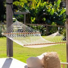Load image into Gallery viewer, Cream rope hammock with wooden spreader bars hanging between timber posts beside a garden