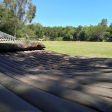 Load image into Gallery viewer, Close-up across the brown quilted hammock bed and matching pillow overlooking a grassy garden