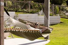 Load image into Gallery viewer, Person relaxing in an olive Whitsunday quilted hammock suspended between timber posts
