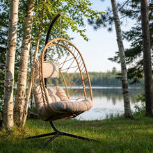Load image into Gallery viewer, Cappuccino Deluxe Nest Chair with steel stand among trees beside a lake.