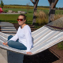 Load image into Gallery viewer, Woman sitting cross-legged in a Dove striped hammock beneath a garden pergola.