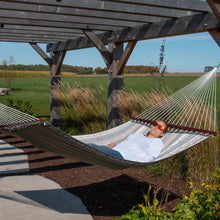 Load image into Gallery viewer, Woman reclining in a Dove striped quilted hammock beneath a wooden pergola.