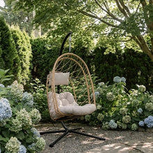 Load image into Gallery viewer, Cappuccino Deluxe Nest Chair with beige cushions and steel stand in a flowering garden.