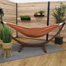 Load image into Gallery viewer, Coral hammock on a solid pine arc stand in a timber-screened space with potted plants and a patterned rug.