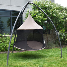 Load image into Gallery viewer, Angled view of a Taupe Cacoon Reto suspended from a grey tripod stand beside garden shrubs