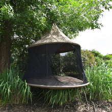 Load image into Gallery viewer, Taupe Cacoon Reto hanging beneath a leafy tree above tall garden plants.