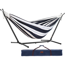 Load image into Gallery viewer, A striped hammock suspended on a black metal stand, shown with a navy blue carrying bag below on a plain white background.