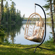 Load image into Gallery viewer, Angled view of the Cappuccino Deluxe Nest Chair with black steel stand between lakeside trees.